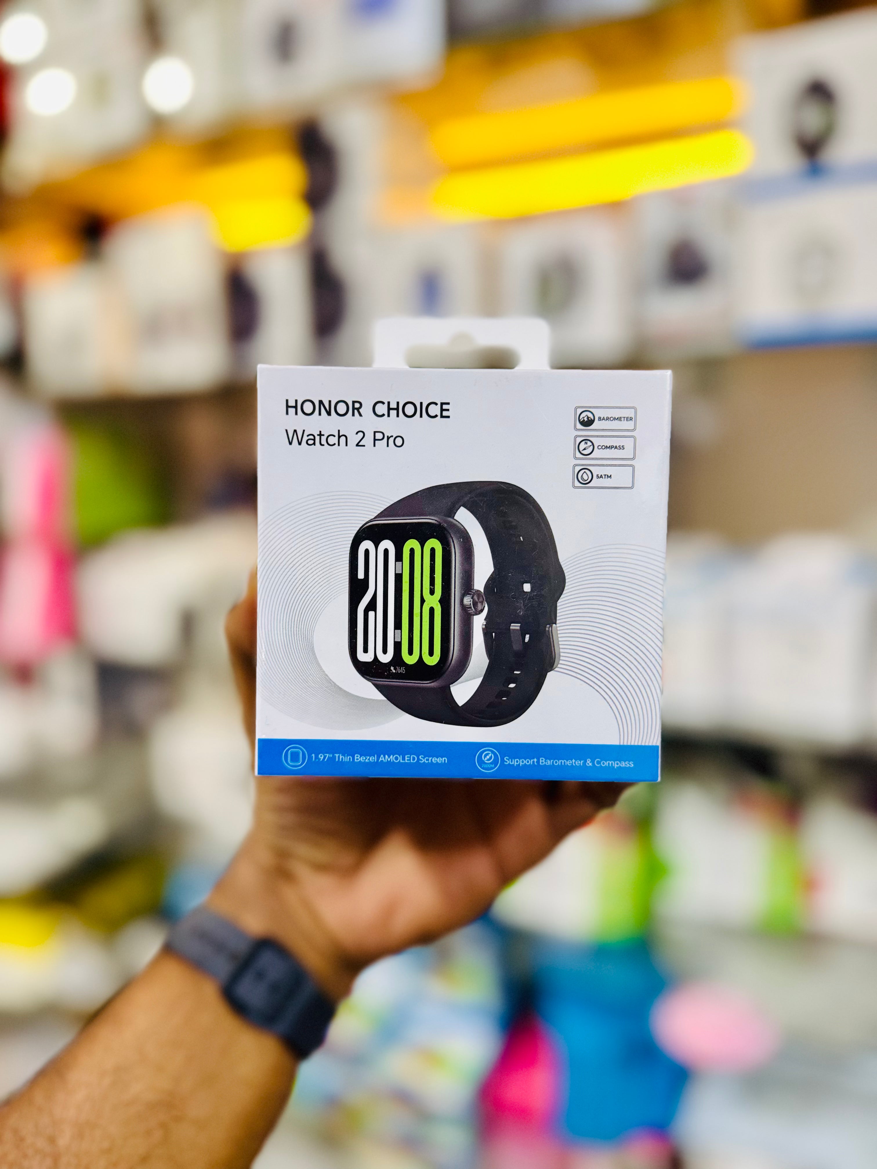 Hand holding a 'Honor Choice Watch 2 Pro' packaging in a store setting